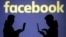 FILE - Silhouettes of laptop users are seen next to a screen projection of Facebook logo in this picture illustration taken March 28, 2018. 
