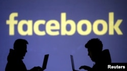 FILE - Silhouettes of laptop users are seen next to a screen projection of Facebook logo in this illustration. 