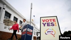 Para pemilih berjalan melintas di depan dua papan referendum bertuliskan 'Ya' dan 'Tidak' di gedung parlemen dalam pelaksanaan referendum hak-hak masyarakat adat di Canberra, Australia, Sabtu, 14 Oktober 2023. (Foto: Tracey Nearmy/Reuters)