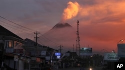 Motorists ride past as Mount Merapi looms in the background, in Sleman, June 25, 2021. Indonesia’s most volatile volcano erupted Friday, releasing plumes of ash high into the air and sending streams of lava with searing gas clouds flowing down its slopes.