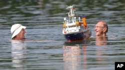 A couple swims beside a model boat in a lake in Ertingen, Germany, Wednesday, June 26, 2019. 