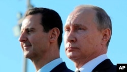 Presiden Rusia Vladimir Putin (kanan) dan Presiden Suriah Bashar Assad menginspeksi barisan pasukan di pangkalan udara Hemeimeem di Suriah, 11 Desember 2017 (Foto: Sputnik, Kremlin Pool Photo via AP/dok)