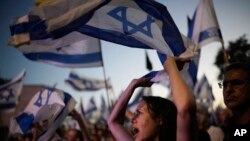 Orang-orang mengibarkan bendera Israel saat melakukan protes terhadap pemerintahan Perdana Menteri Israel Benjamin Netanyahu dan menuntut pemilihan umum di luar Knesset, parlemen Israel, di Yerusalem, Selasa, 18 Juni 2024. (Foto: AP)