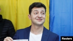 Ukrainian presidential candidate Volodymyr Zelenskiy holds up his ballot while standing in front of the media at a polling station during the second round of a presidential election in Kyiv, Ukraine, April 21, 2019. 