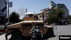 An Afghan police officer takes cover as smoke rises from the site of a suicide bomber attack in Kabul, Afghanistan, July 31, 2017.