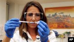Dr Felicity Hartnell, who is a clinical research fellow at Oxford University, holds a vial of an experimental vaccine against Ebola in Oxford, England Wednesday Sept. 17, 2014. A former nurse will be the first of 60 healthy volunteers in the UK who will receive the vaccine. The vaccine was developed by the U.S. National Institutes of Health and GlaxoSmithKline and targets the Zaire strain of Ebola, the cause of the ongoing outbreak in West Africa. A trial of the same vaccine has already begun in the U.S. (AP Photo/Steve Parsons/Pool)