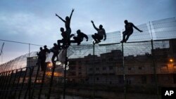 FILE - Sub-Saharan migrants climb over a metallic fence that divides Morocco and the Spanish enclave of Melilla, March 28, 2014. 