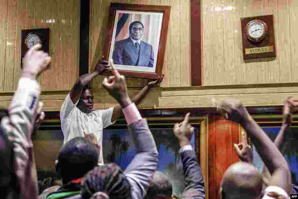 People remove the portrait of former Zimbabwean President Robert Mugabe from the wall at the International Conference center, after his resignation, Nov. 21, 2017 in Harare.