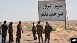 Foto yang dirilis 3 September 2017 oleh kantor berita resmi Suriah SANA, menunjukkan pasukan Suriah dan pria bersenjata pro-pemerintah yang berdiri di samping sebuah plakat dalam bahasa Arab yang berbunyi, "Deir Ezzor menyambut Anda," di kota timur Deir Ezzor, Syria.