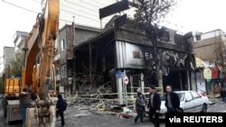 People walk near a burned bank after protests against increased fuel prices in Tehran, Iran, Nov. 20, 2019.