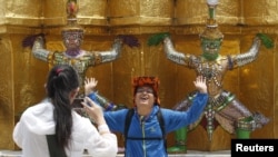 Seorang wisatawan China berpose dengan gaya mirip patung yang dipamerkan di Grand Palace, Bangkok, 23 Maret 2015. (Foto: dok).