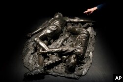 A woman looks at a bronze sculpture by Kehinde Wiley titled "Death of Two Soldiers," at the de Young Museum in San Francisco, March 24, 2023. The sculpture is part of the "Kehinde Wiley: An Archaeology of Silence," exhibition. (AP Photo/Godofredo A. Vásquez)