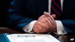 FILE - President Donald Trump finishes signing the coronavirus stimulus relief package in the Oval Office at the White House in Washington, March 27, 2020. The first relief checks for Americans started arriving in their bank accounts April 15.