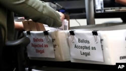FILE - A Miami-Dade County Elections Department employee places a vote-by-mail ballot for the August 18 primary election into a box for rejected ballots at the Miami-Dade County Elections Department, in Doral, Florida, July 30, 2020.