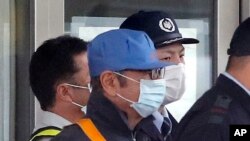 Pria mengenakan masker bertopi biru, diyakini mantan Ketua Nissan Carlos Ghosn, dikawal penjaga keamanan keluar dari Pusat Penahanan Tokyo di Tokyo, Rabu, 6 Maret 2019, setelah membayar uang jaminan sebesar 1 miliar yen ($ 8,9 juta). 