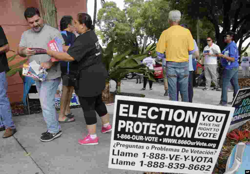 Ingrid Vaca, of Falls Church, Virginia, a volunteer with Election Protection, second from left, hands a voter a leaflet informing him about voter&#39;s rights, outside of a polling station at the Miami-Dade County Auditorium, in Miami, Florida.