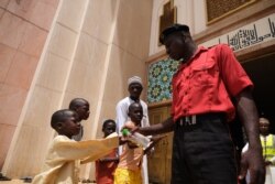 A security official dispenses hand sanitizer to worshippers at the National Mosque in Abuja, Nigeria, March 20, 2020. Nigeria said Thursday it would shut schools and limit religious meetings in Lagos and Abuja.