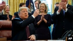 President Donald Trump holds up a pen during a signing ceremony of the "Cybersecurity and Infrastructure Security Agency Act," in the Oval Office of the White House, Nov. 16, 2018, in Washington.