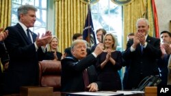 President Donald Trump holds up a pen during a signing ceremony of the "Cybersecurity and Infrastructure Security Agency Act," in the Oval Office of the White House, Nov. 16, 2018, in Washington.