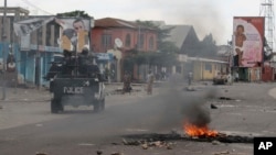 Kendaraan polisi melewati sampah yang dibakar dalam protes-protes di Kinshasa, Republik Demokratik Kongo (20/12). (AP/John Bompengo)