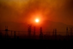 FILE - Smoke from the Saddleridge Fire hangs above power lines as the sun rises in Newhall, California, Oct. 11, 2019.