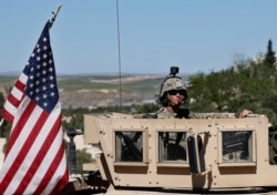 FILE - A U.S. soldier sits in an armored vehicle on a road leading to the tense front line with Turkish-backed fighters, in Manbij, north Syria, April 4, 2018.