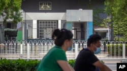 People wearing face masks to protect against the new coronavirus ride past the Australian Embassy in Beijing, June 6, 2020. 