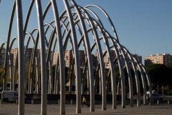 A woman wearing a face mask to protect against the spread of coronavirus walks beneath the metal Puerta de la Ilustracion urban sculpture designed by Andreu Alfaro in Madrid, Spain, Oct. 15, 2020.