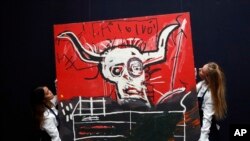 Sotheby employees hang up the acrylic and oilstick on canvas painting, Cabra by Jean-Michel Basquiat at Sotheby's auction house in London, Friday, Oct. 6, 2017 ahead of New York sales for Contemporary, Impressionist & Modern Art by Monet, Cèzanne, Miró, Magritte, Picasso, Basquiat, Dubuffet & Lichtenstein. The painting is estimated to fetch US$9-12 million.