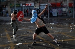 A demonstrator uses a stop sign as protection as another throws stones during a protest against Chile's government in Santiago, Chile, Oct. 29, 2019.