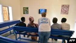 FILE - A UNHCR representative (C) speaks with refugees as they watch television in a waiting room of a UNHCR office in Niamey, Niger, Nov. 17, 2017, after being evacuated from Libya.