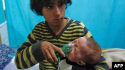 A Syrian boy holds an oxygen mask over the face of an infant at a makeshift hospital following a reported gas attack on the rebel-held besieged town of Douma in the eastern Ghouta region on the outskirts of the capital Damascus, Jan. 22, 2018. (AFP PHOTO / HASAN MOHAMED)