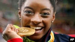 United States' Simone Biles bites her gold medal for the artistic gymnastics women's individual all-around final at the 2016 Summer Olympics in Rio de Janeiro, Brazil, Aug. 11, 2016.