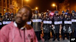 បាតុករ​ម្នាក់​បាន​ដើរ​ឆ្លង​កាត់​ប៉ូលិស ​ខណៈ​ដែល​ពួក​គេ កំពុង​តែ​ពង្រឹង​ បំរាម​គោចរ​នៅ​យប់​ទី​បី នា​ថ្ងៃ​ទី​ ៣០ ខែ​មេសា​ ឆ្នាំ​២០១៥ ​នៅ​ក្នុង​ទី​ក្រុង Baltimore។