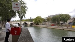 Seorang wartawan berpose di dekat tempat BAK ramah lingkungan yang dicat merah di Ile Saint-Louis di pinggiran Sungai Seine, Paris, Perancis, 13 Agustus 2018.
