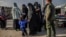 FILE - Veiled women, reportedly wives and members of the Islamic State, walk under the supervision of a fighter from the Syrian Democratic Forces at the al-Hol camp in al-Hasakah governorate in northeastern Syria, Feb. 17, 2019.
