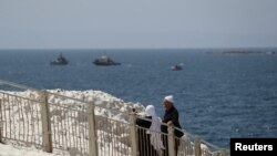 Sejumlah warga tampak berjalan di tepi pantai di wilayah Rosh Hanikra, dekat perbatasan Lebanon, ketika kapal angkatan laut Israel terlihat berlayar di laut Mediterania, pada 4 Mei 2021. (Foto: Reuters/Ammar Awad)