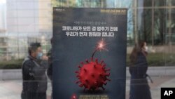 Para pejalan kaki mengenakan masker melewati poster kesadaran menjaga jarak sosial di tengah pandemi COVID-19, di Seoul, Korea Selatan, 7 Desember 2020. (Foto: dok).
