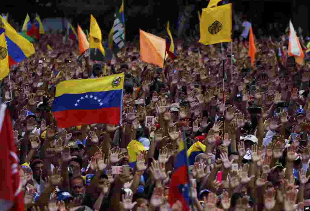 Anti-government protesters hold their hands up during the symbolic swearing-in of Juan Guaido, head of the opposition-run congress, who declared himself interim president of Venezuela during a rally demanding President Nicolas Maduro's resignation in Caracas.