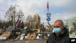 Seorang pria bermasker berdiri di depan barikade dan bendera Rusia dan Soviet di pintu masuk gedung pemerintah di Luhansk, Ukraina (9/4). (AP/Igor Golovniov)