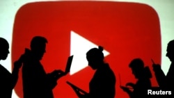 FILE PHOTO: Silhouettes of laptop and mobile device users are seen next to a screen projection of the YouTube logo in this picture illustration taken March 28, 2018. 