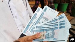 Seorang pria menunjukkan uang kertas baru yang dicetak dengan potret Jenderal Aung San, mendiang ayah pemimpin Myanmar Aung San Suu Kyi, di luar Bank Ekonomi Myanmar Selasa, 7 Januari 2020, di Yangon, Myanmar. (Foto: AP)