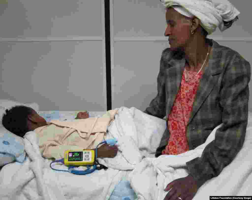 Family member watches young child recover from essential surgery, safety monitored.