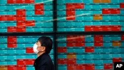 FILE - A man walks past an electronic stock board showing Japan's Nikkei 225 index at a securities firm in Tokyo, Japan, April 8, 2020.