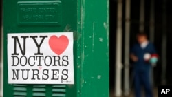 A sign acknowledging the work of doctors and nurses is posted on a traffic control box outside Brooklyn Hospital Center, as a hospital worker, right, waits for a traffic light to change before reporting to duty, Sunday, April 5, 2020, in New York.