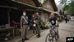 Seorang migran Karen yang tinggal di Thailand bersepeda melewati polisi Thailand di kota Mae Sam Laep di sisi sungai Salween di Thailand di provinsi Mae Hong Son pada 2 April 2021, di seberang tempat pengungsi Myanmar sebelumnya berusaha melintasi perbatasan Thailand. (Foto: AFP)