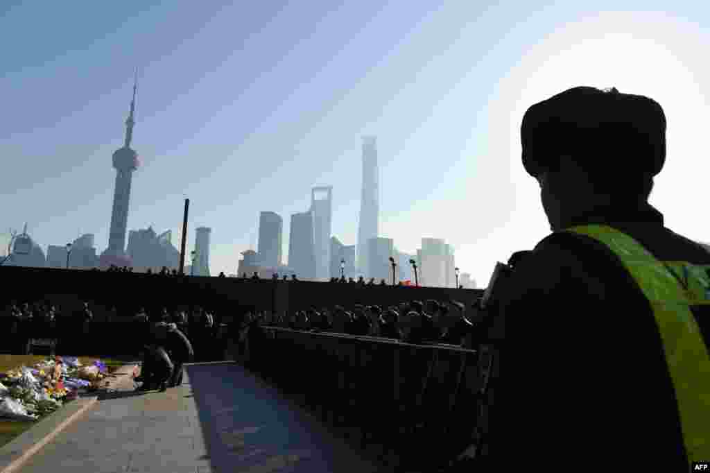 Seorang petugas keamanan tampak mengawasi, sementara orang-orang yang berkabung meletakkan bunga dan membakar dupa di lokasipara korban yang tewas terinjak pada malam tahun baru di Bund di Shanghai, China. Bencana malam tahun baru itu terjadi sesaat sebelum tengah malam di wilayah bersejarah di kota itu, menewaskan setidaknya 36 orang. &nbsp;