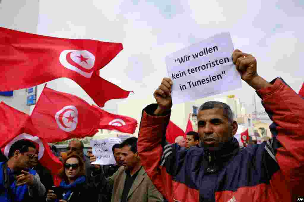 Tunisians wave banners and their national flag during a demonstration in Midoun, northeast of Djerba, two days after gunmen attacked the National Bardo Museum. The attack which killed 21 people, was the country&#39;s worst since the 2011 uprising that toppled leader Zine El Abidine Ben Ali. German writting on placard reads: &quot;We don&#39;t want any terrorists in Tunisia.&quot;