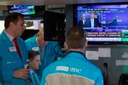 FILE - Traders at the New York Stock Exchange listen to President Donald Trump's televised White House news conference, March 17, 2020.