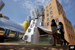 FILE - People walk past the Ray and Maria Stata Center, behind, on the campus of Massachusetts Institute of Technology, in Cambridge, Mass. July 16, 2019. (AP Photo/Steven Senne)